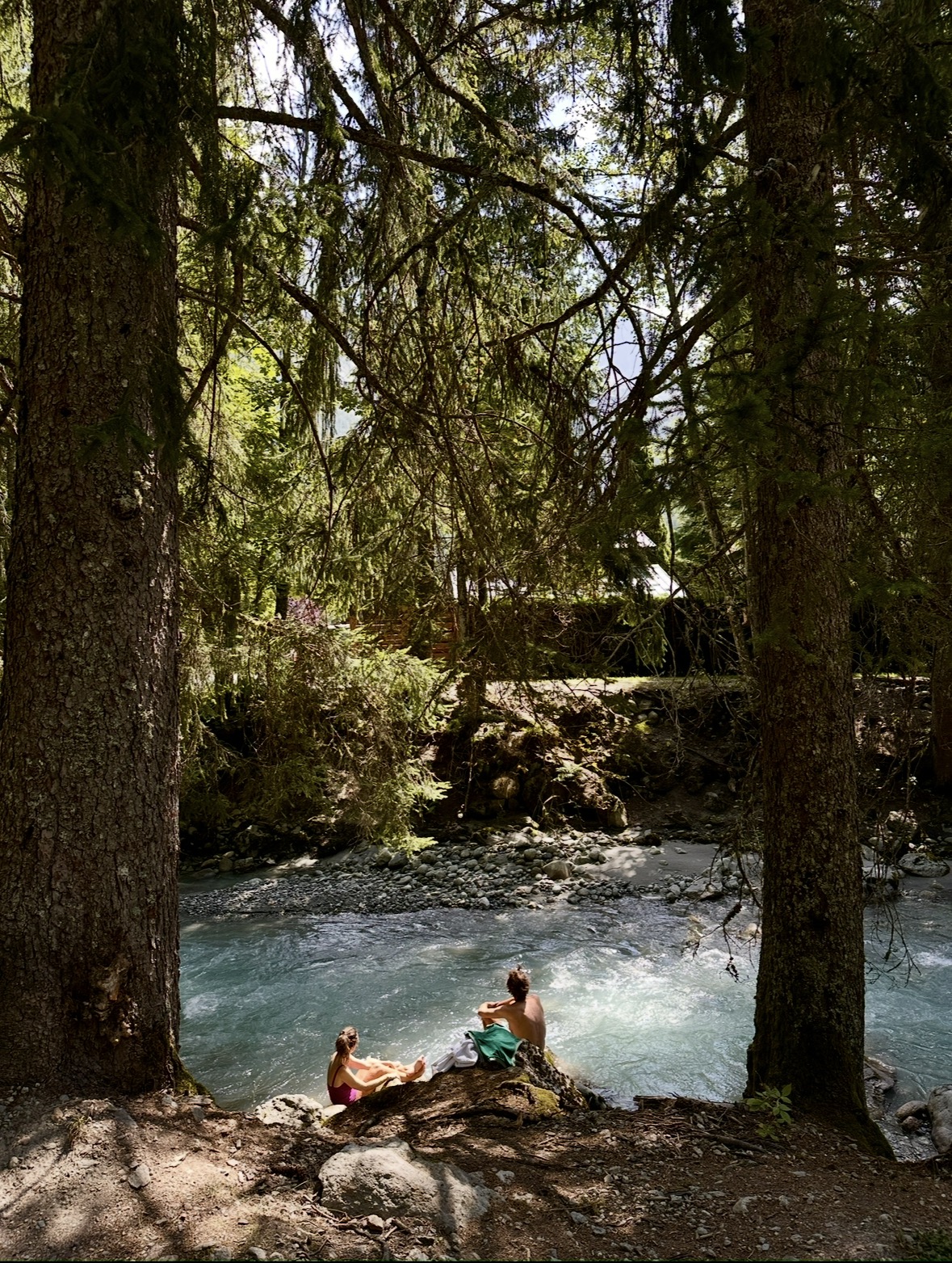 Due persone sedute insieme sulla riva di un fiume, tra gli alberi